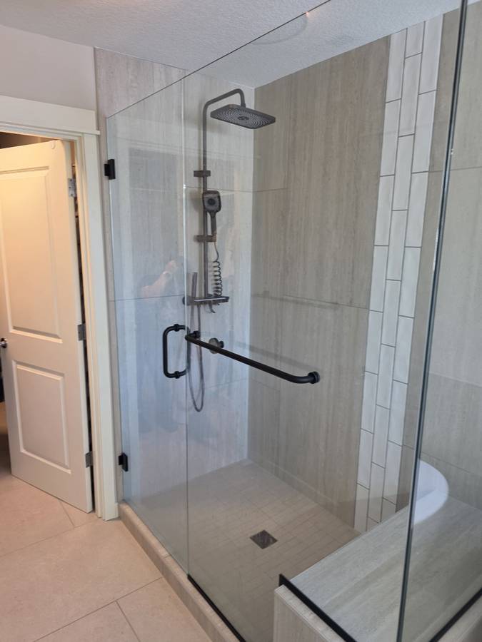 Glass shower enclosure with tile walls, a handrail and shower fixtures